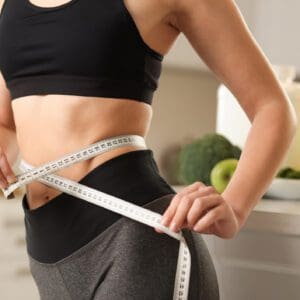 Woman measuring waist with tape in kitchen.